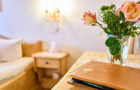 Hotelzimmer mit einer Vase frischer Blumen und einem Menübuch auf dem Tisch, ideal für einen entspannten Familienurlaub.