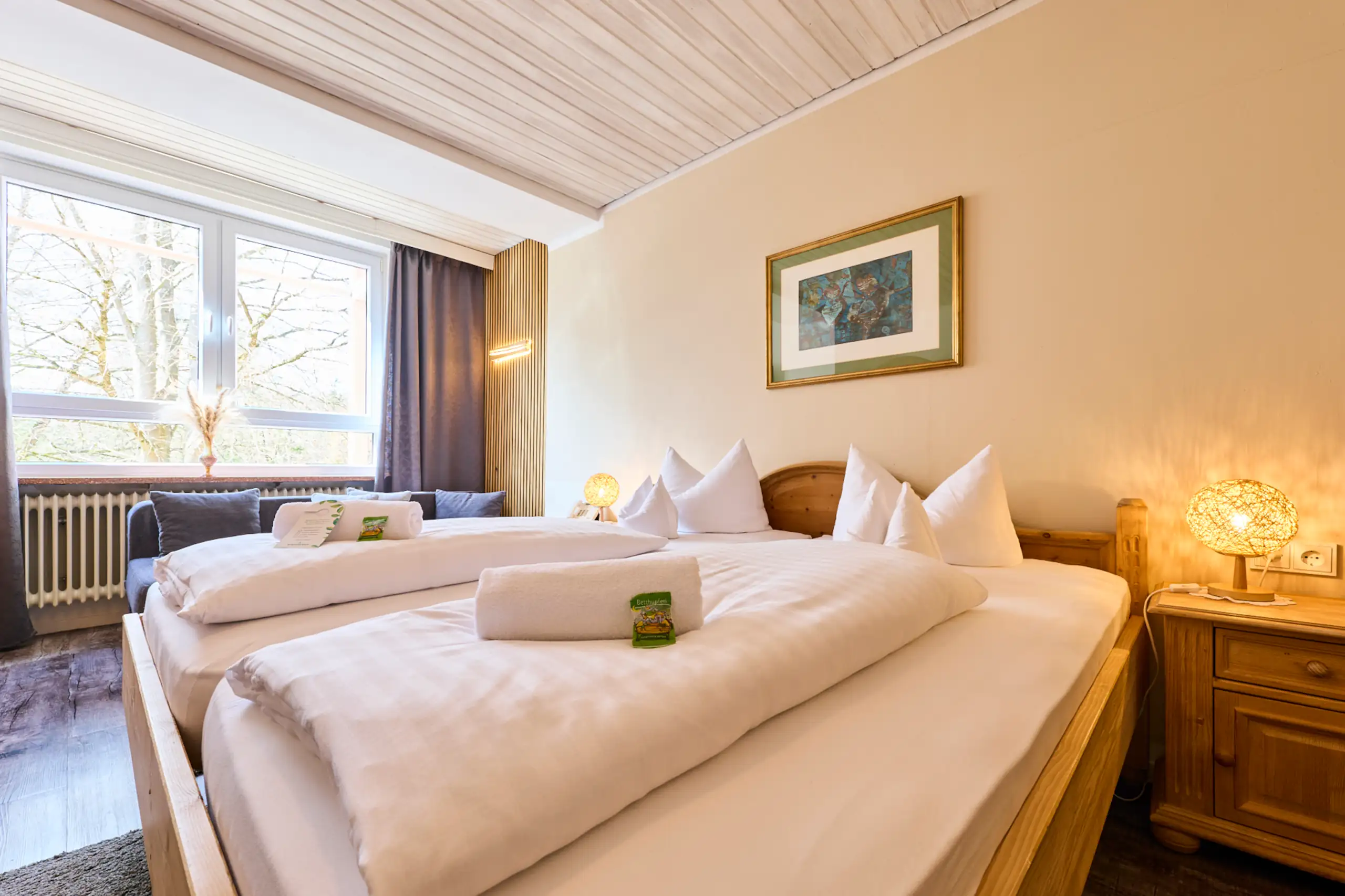 Ein modernes Zimmer im Hotel Alpenglück mit zwei Betten, gemütlichem Sofa und einer großen Fensterfront, ideal für Familien.