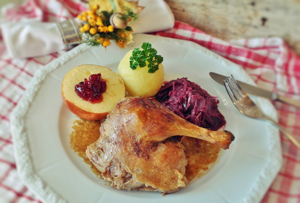 Ein festliches Gericht mit knuspriger Ente, Apfel, Kartoffelknödel und Rotkohl, ideal für Familienessen in der Weihnachtszeit.