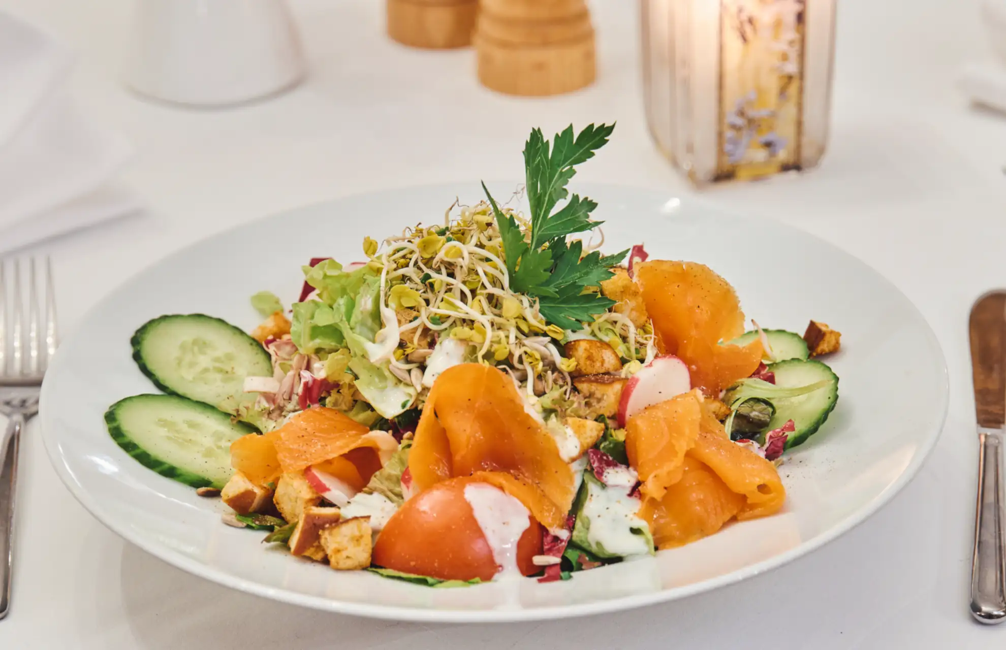 Ein bunter Salat mit Räucherlachs, Gurken, Tomaten und frischen Sprossen im Restaurant, ideal für ein gesundes Mittagessen.