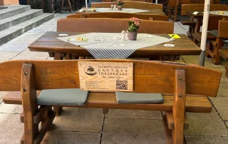 Holzbank im Biergarten mit Tisch und Blumendekoration, ideal für gemütliche Stunden während eines Familienausflugs oder im Urlaub.