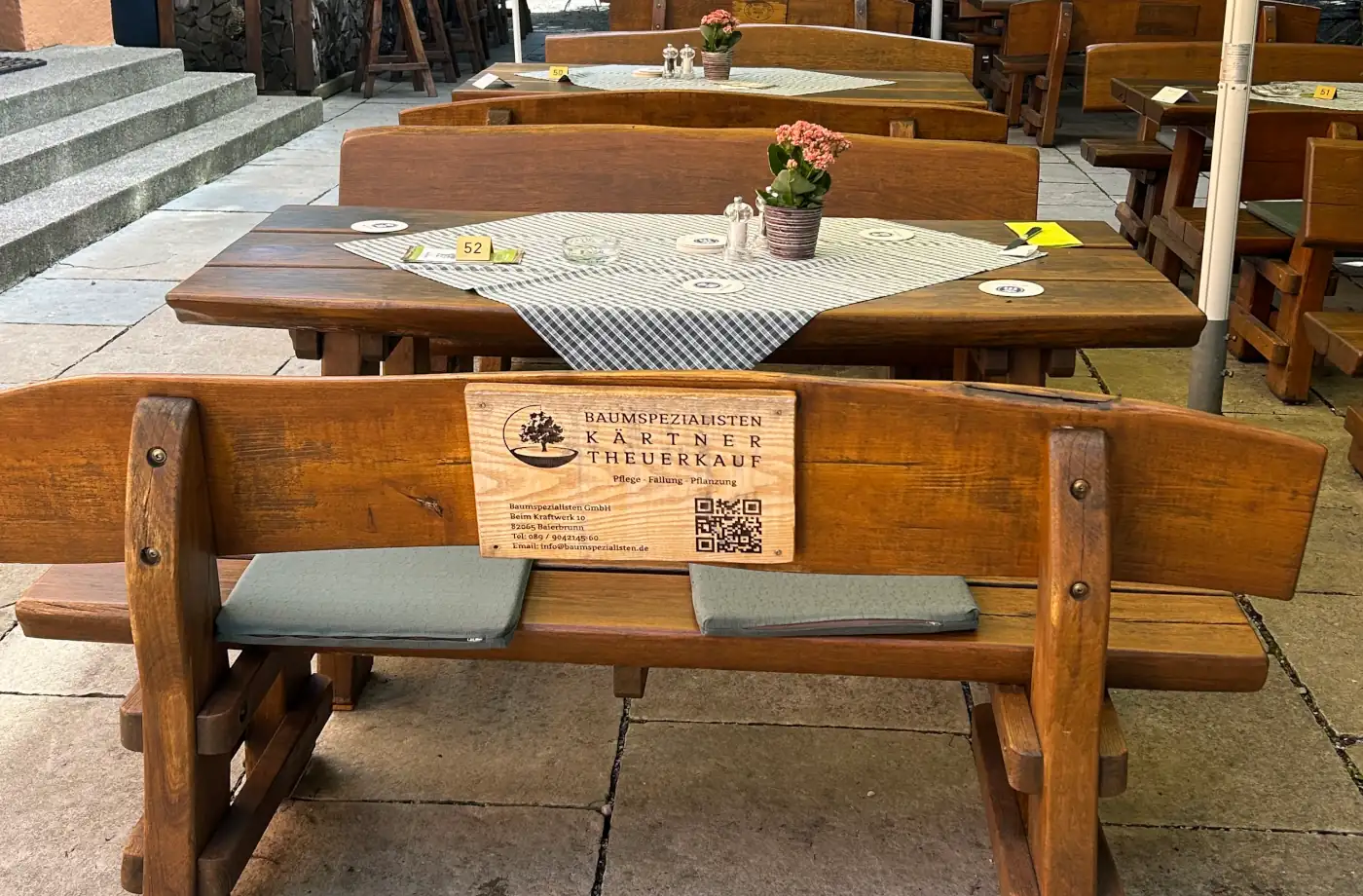 Holzbank im Biergarten mit Tisch und Blumendekoration, ideal für gemütliche Stunden während eines Familienausflugs oder im Urlaub.