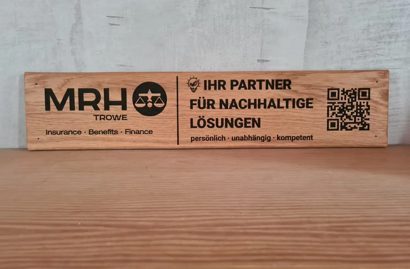 Holzschild von MRH Trowe mit Informationen zu Versicherungen, Benefits und Finanzen, sowie einem QR-Code für mehr Informationen.