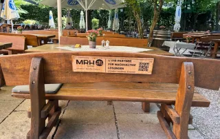 Holztisch und Bänke im Außenbereich eines Restaurants, dekoriert mit Blumen und einem QR-Code für nachhaltige Services.