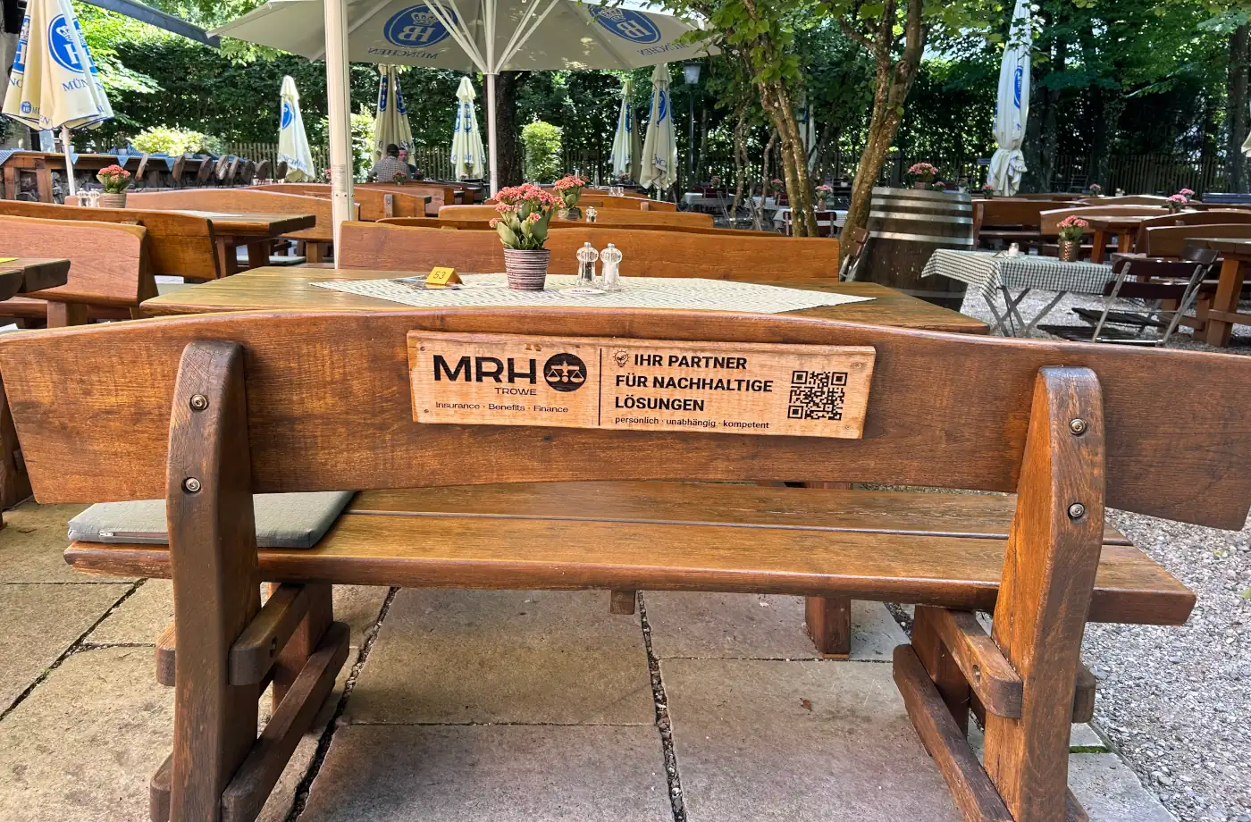 Holztisch und Bänke im Außenbereich eines Restaurants, dekoriert mit Blumen und einem QR-Code für nachhaltige Services.