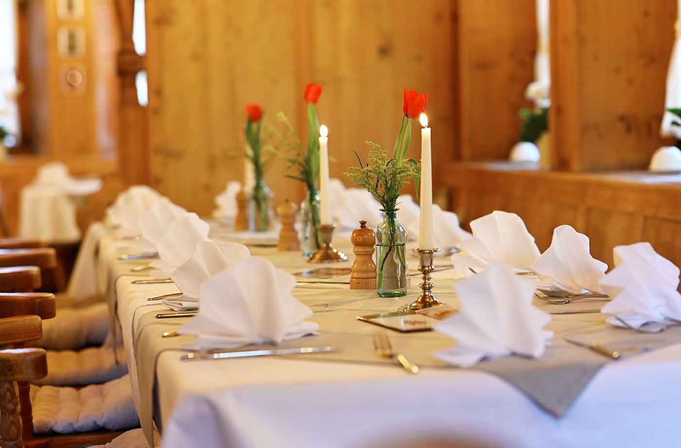 Tisch im rustikalen Restaurant, liebevoll dekoriert mit weißen Servietten, Kerzen und frischen Blumen für ein romantisches Dinner.