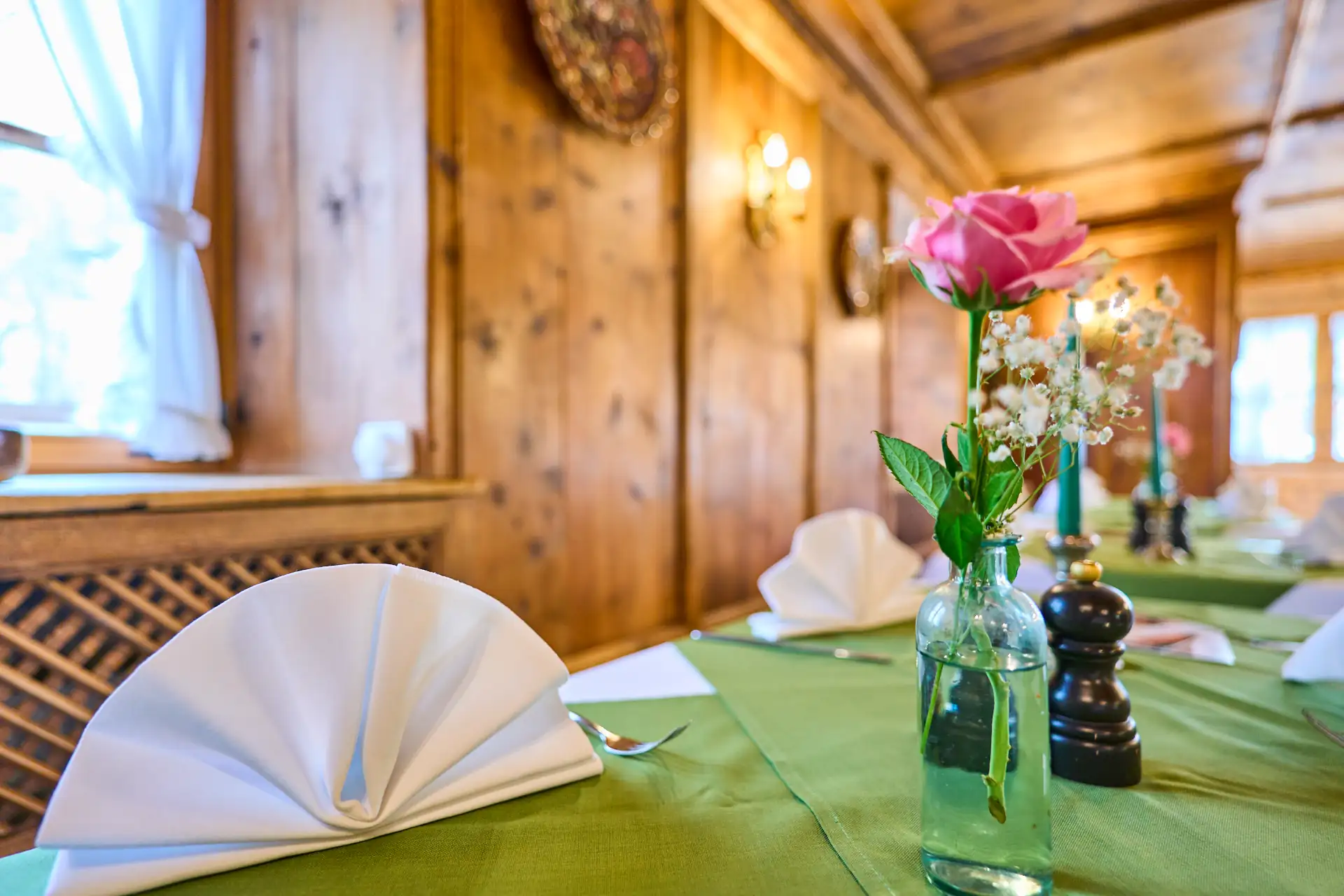 Tischdekoration im Restaurant mit weißen Servietten, Blumen in einer Flasche und dicker Holzvertäfelung für ein einladendes Essen.