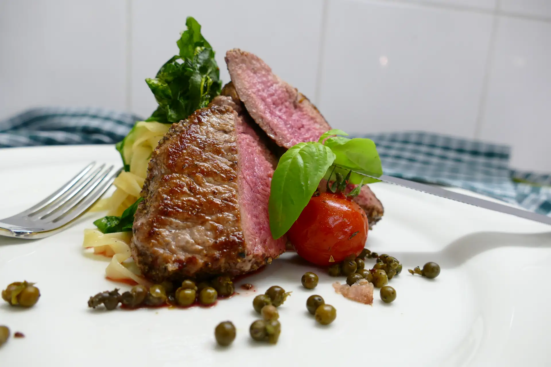 Ein perfekt gegrilltes Rindersteak mit frischem Basilikum und Tomate, serviert auf einem Teller beim gehobenen Essen.
