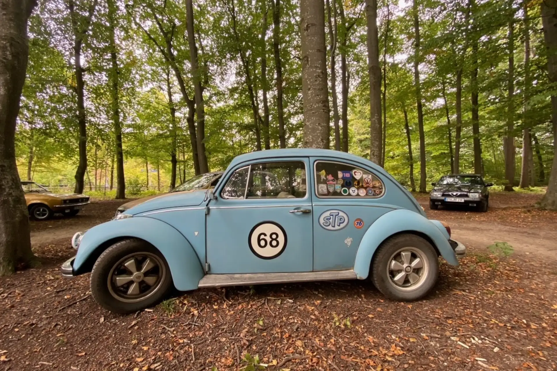 Ein blauer Volkswagen Käfer steht im Wald, umgeben von Bäumen, perfekt für Autoliebhaber und Naturfreunde.