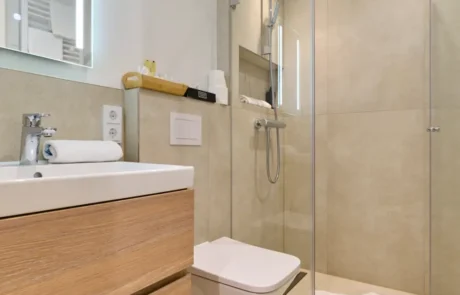 Moderne Badgestaltung im Hotel mit eleganter Dusche und Holzdetails Funktionales Badezimmer im Hotel mit eleganter Dusche, Holzbadmöbel und frischen Handtüchern, ideal für den Familienurlaub.