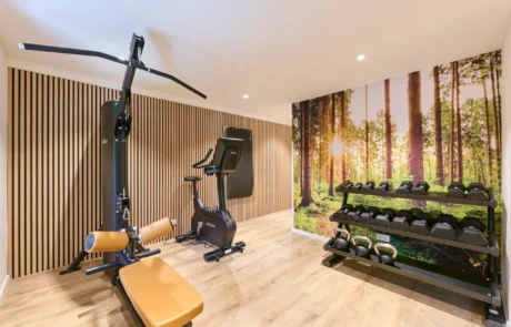 Modernes Fitnessstudio im Hotel mit hochwertiger Ausstattung für aktiven Urlaub Fitnessraum im Hotel mit einem Gewichtheber, einem Fahrrad und einer Wand mit Waldmotiv, ideal für Gesundheitsbewusste im Urlaub.