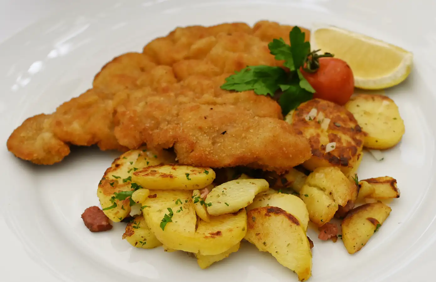 Ein köstliches Wiener Schnitzel serviert mit goldenen Bratkartoffeln, Zitrone und einem kleinen Tomatenstück, ideal für Feinschmecker.